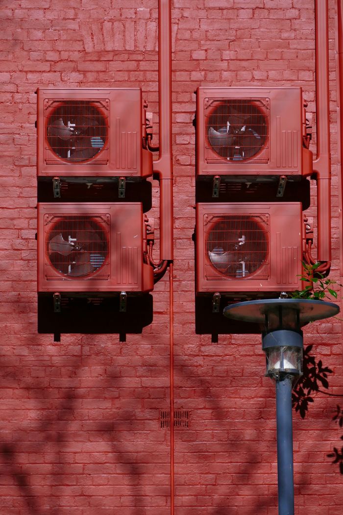 Red air conditioning units on a red brick wall in Adelaide, emphasizing urban architecture.