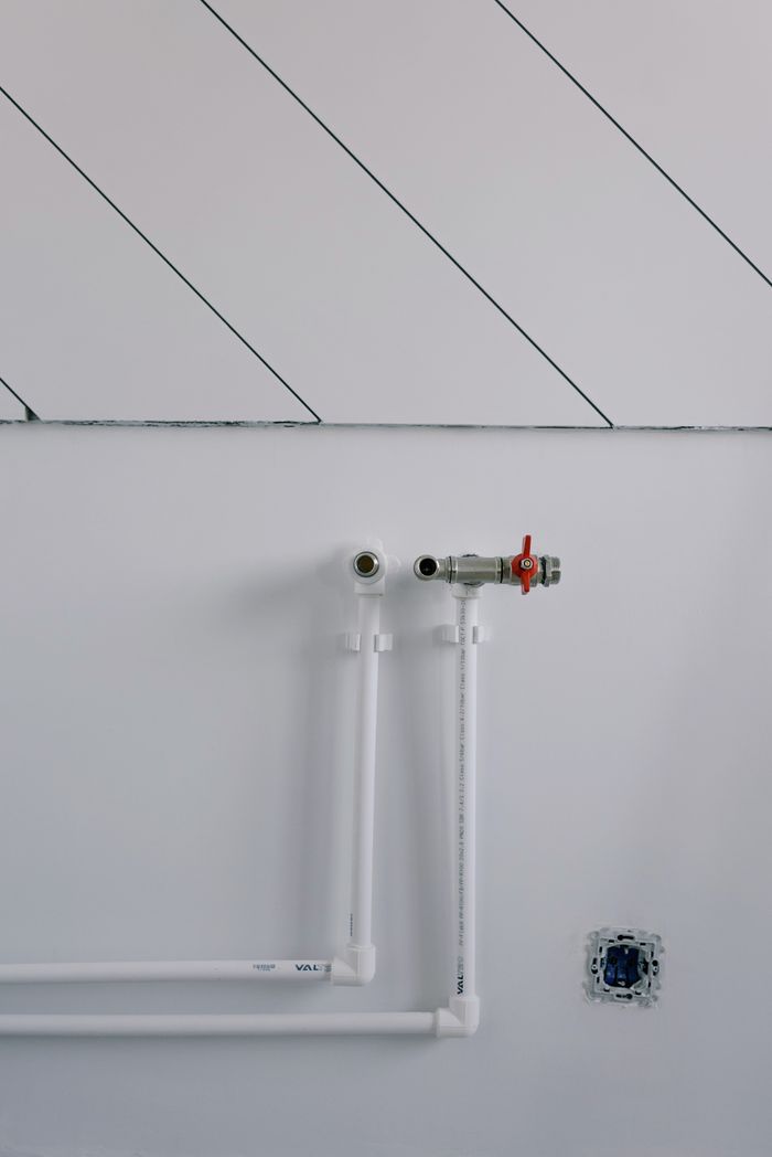 Long thin black slanted lines over pipes of radiator casting shadow on white wall in daytime